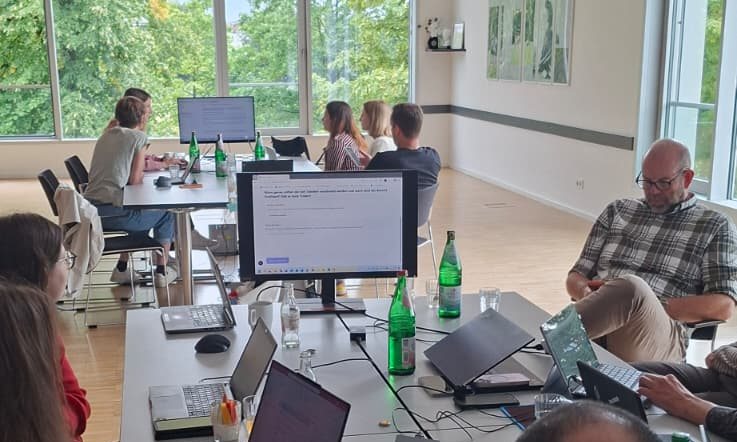 Teilnehmende an langen Tischreihen mit Laptops